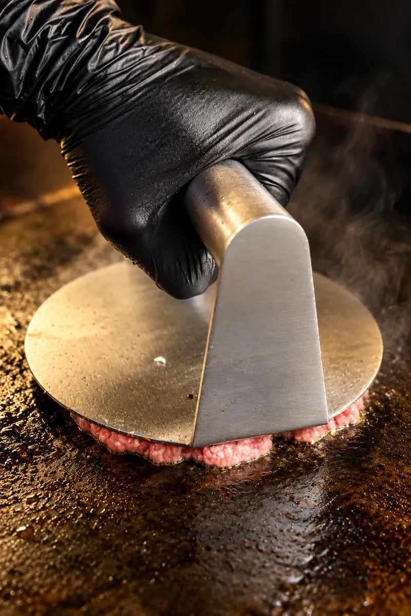 La pressa schiaccia la carne sulla piastra rovente